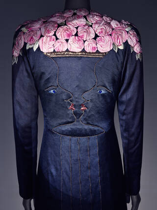 Black coat with shoulders covered in pink roses and two faces stitched down the back