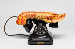 Black vintage telephone with dial and earpiece with orange lobster on top of the earpiece