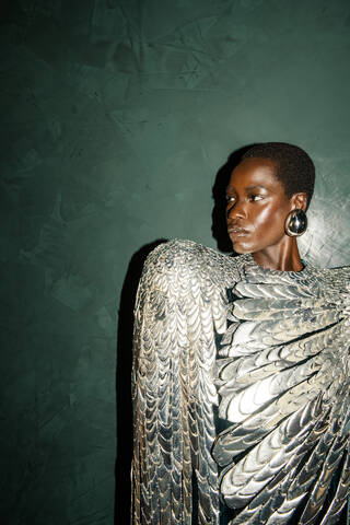 woman standing against a dark green background wearing a silver dress that looks like feathers